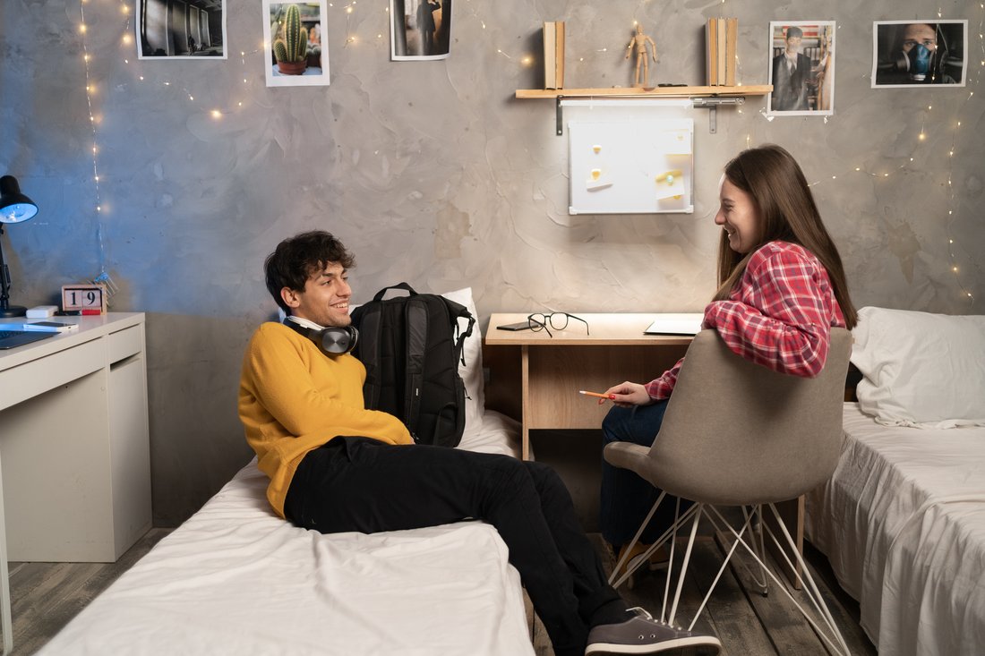Dwoje studentów rozmawia w pokoju w akademiku z łóżkami i biurkiem