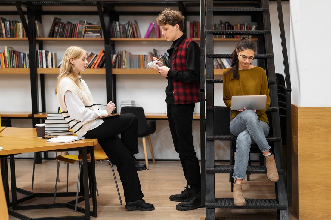 Troje studentów uczy się w jasnej strefie nauki przy regałach z książkami